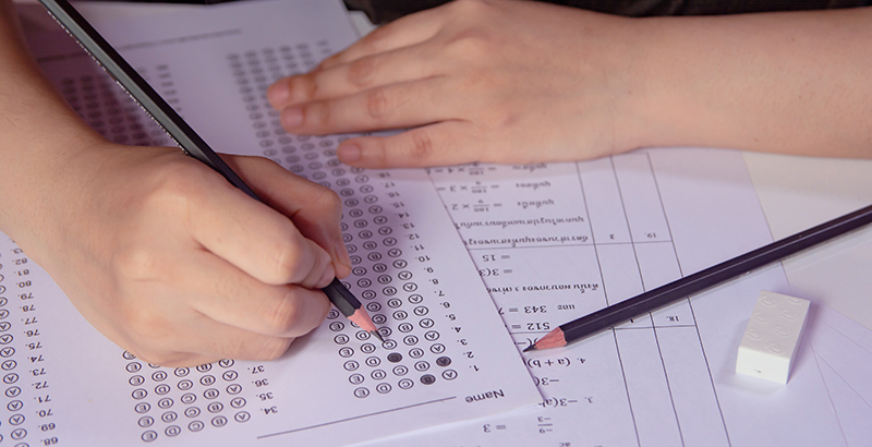 Students hand holding pencil writing selected choice on answer sheets and Mathematics question sheets. students testing doing examination. school exam